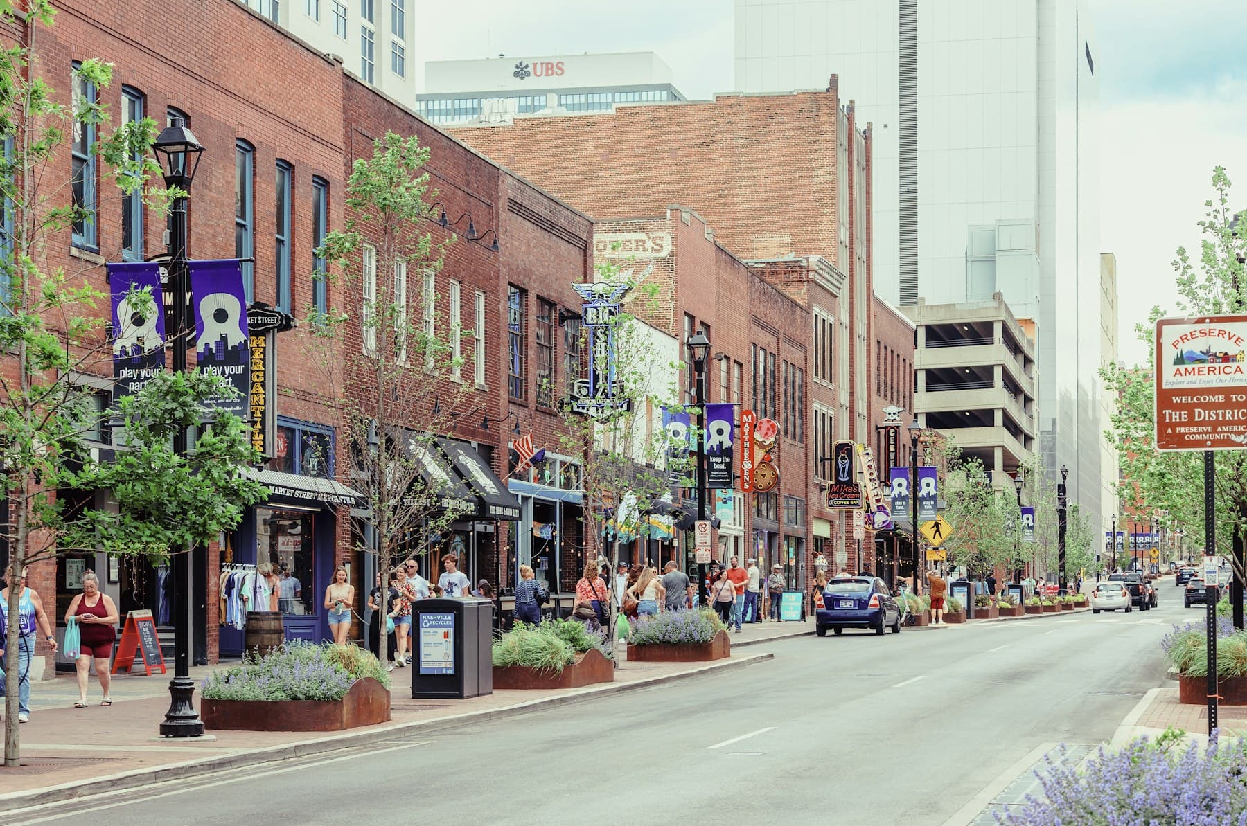 Pedestrians exploring a tree-lined Nashville street with brick storefronts